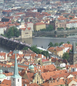 Panoramic high-angle view of the historic Charles Bridge over the Vltava River, surrounded by terracotta tile roofs in Prague