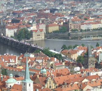 Panoramic high-angle view of the historic Charles Bridge over the Vltava River, surrounded by terracotta tile roofs in Prague