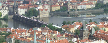Panoramic high-angle view of the historic Charles Bridge over the Vltava River, surrounded by terracotta tile roofs in Prague