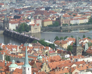 Panoramic high-angle view of the historic Charles Bridge over the Vltava River, surrounded by terracotta tile roofs in Prague