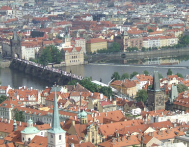 Panoramic high-angle view of the historic Charles Bridge over the Vltava River, surrounded by terracotta tile roofs in Prague