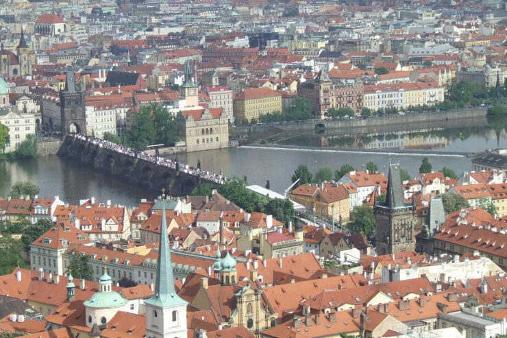 Panoramic high-angle view of the historic Charles Bridge over the Vltava River, surrounded by terracotta tile roofs in Prague