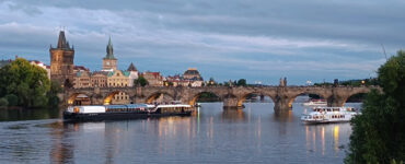 Prague river cruise on the Vltava River at sunset with Charles Bridge, sightseeing boats and the historic Old Town skyline.