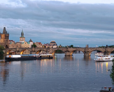 Prague river cruise on the Vltava River at sunset with Charles Bridge, sightseeing boats and the historic Old Town skyline.